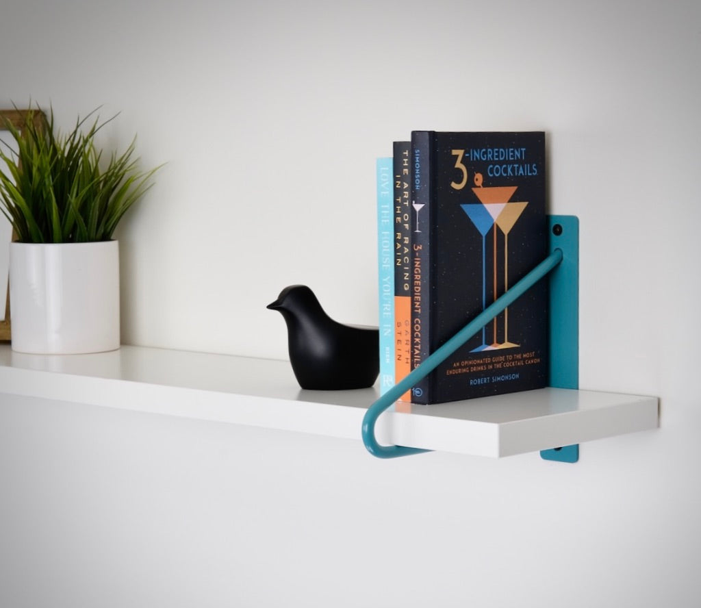 Blue two rod hairpin shelf brackets with a white shelf holding books, plant and picture frame.